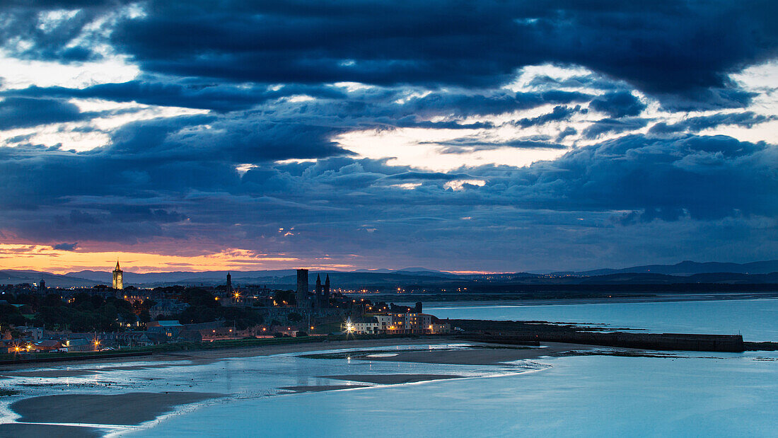 Looking across the bay to St. Andrews harbour and pier with the sun setting beyond the city as dusk falls, St. Andrews, Fife, Scotland, United Kingdom, Europe