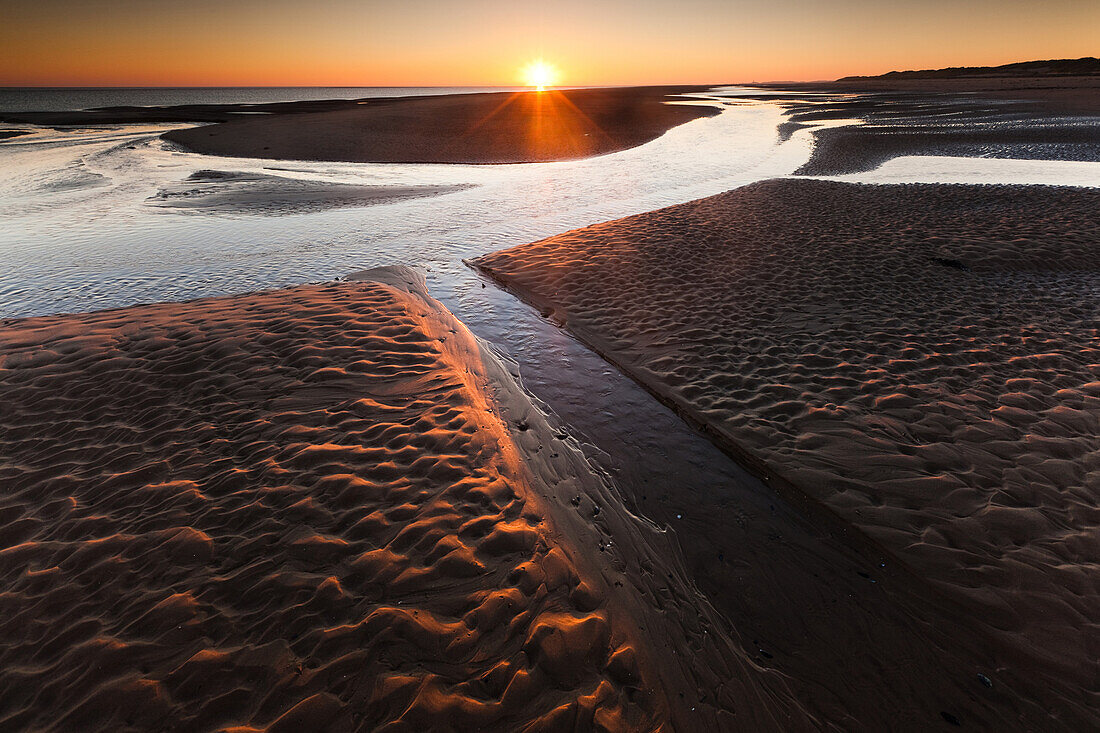 Sonnenuntergang über Strandströmen und Sandbecken am Llanddwyn Strand bei sehr Ebbe, West Anglesey, Wales, Großbritannien, Europa