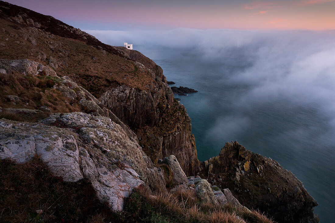 A temporary clearing in thick fog during a temperature inversion over the Irish Sea at dusk, South Stack, RSPB tower on clifftop, Anglesey, Wales, United Kingdom, Europe