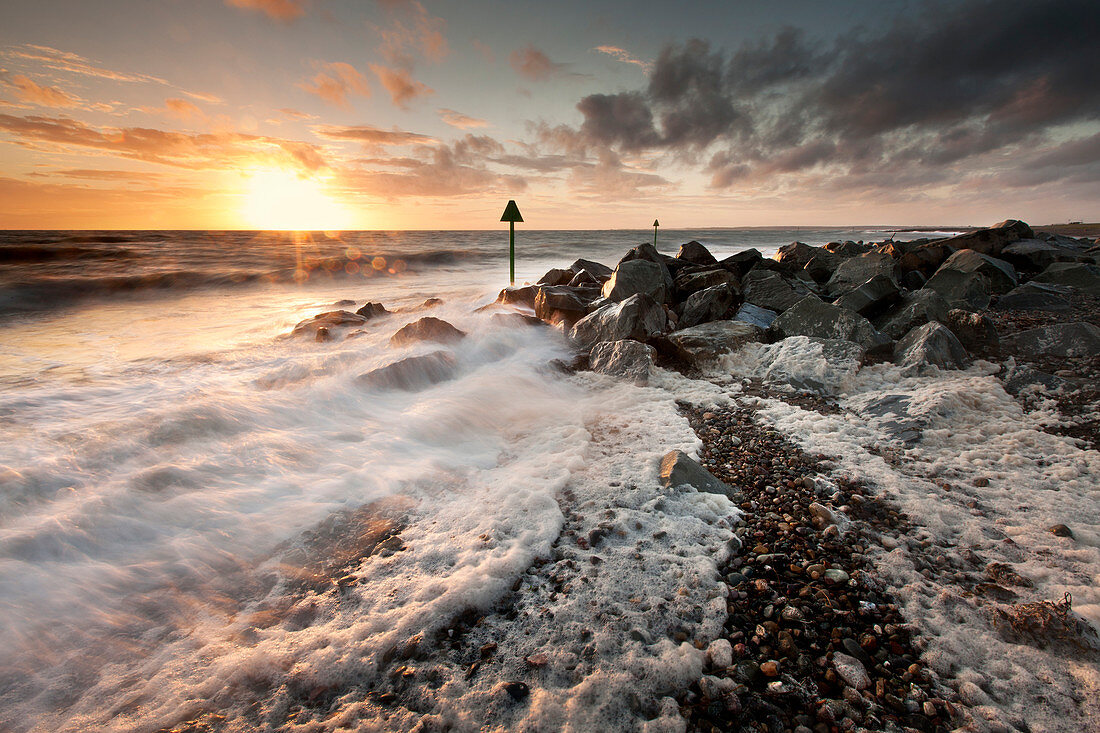 Gale driven surf and foam pile onto a shingle beach at sunset at Dinas Dinlle, Llyn Peninsula, Gwynedd, Wales, United Kingdom, Europe