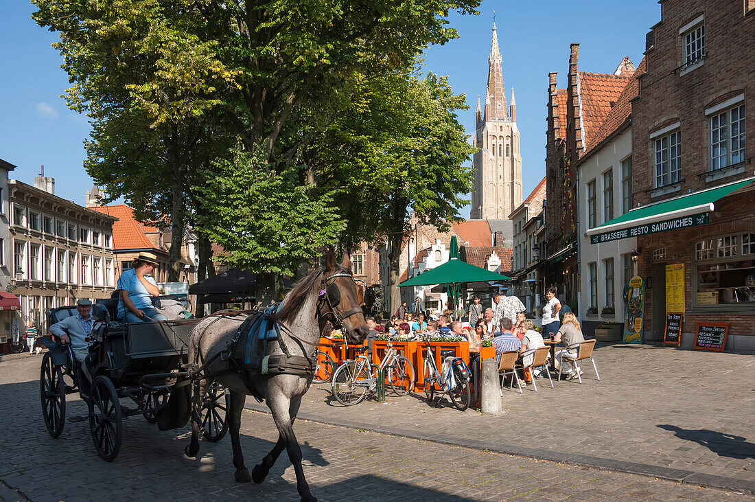 Square with cafe, horse and carriage, and spire of Church of Our Lady, Bruges, Belgium, Europe
