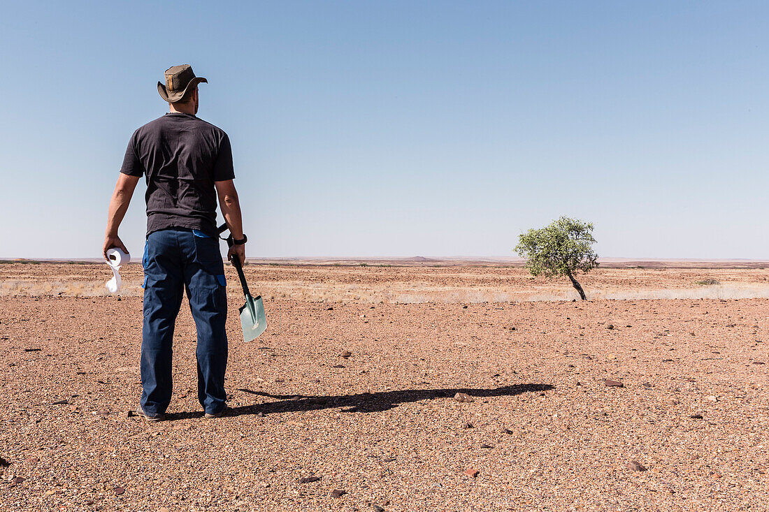 A man reflecting upon his toilet options. What's not buried carefully, will be dug out by wild animals, and due to the dry climate, things decompose extremely slowly. Paper has to be burned. Damaraland, Erongo, Namibia, Africa