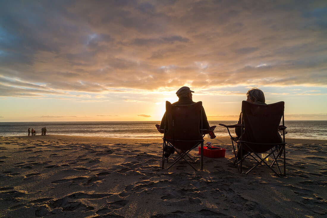 Paar sitzt in Campingstühlen am Strand, beobachtet Sonnenuntergang, Horizont, Romantik, Entspannung, Hokitika, Bier, Westküste, Südinsel, Neuseeland