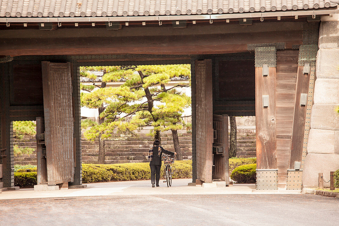 Dame mit Fahrrad betritt Garten des Kaiserpalast über das Tor Hirakawamon, Chiyoda-ku, Tokio, Japan