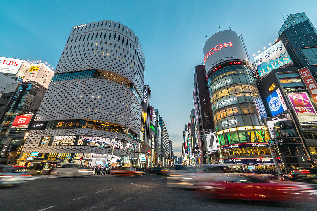 Kreuzung mit bewegen Autos am Ginza Place und Ricoh Imaging Square in der Ginza während der blauen Stunde, Chuo-ku, Tokio, Japan