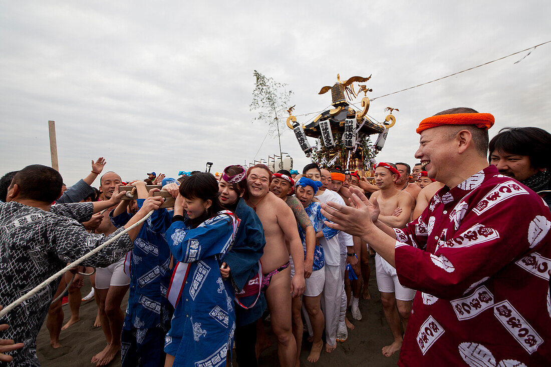 Männer im Fundoshi und Frauen im Yukata tragen einen Omikoshi während des Seijin-Sai-Fest am Enoshima Strand, Fujisawa, Kanagawa Präfektur, Japan