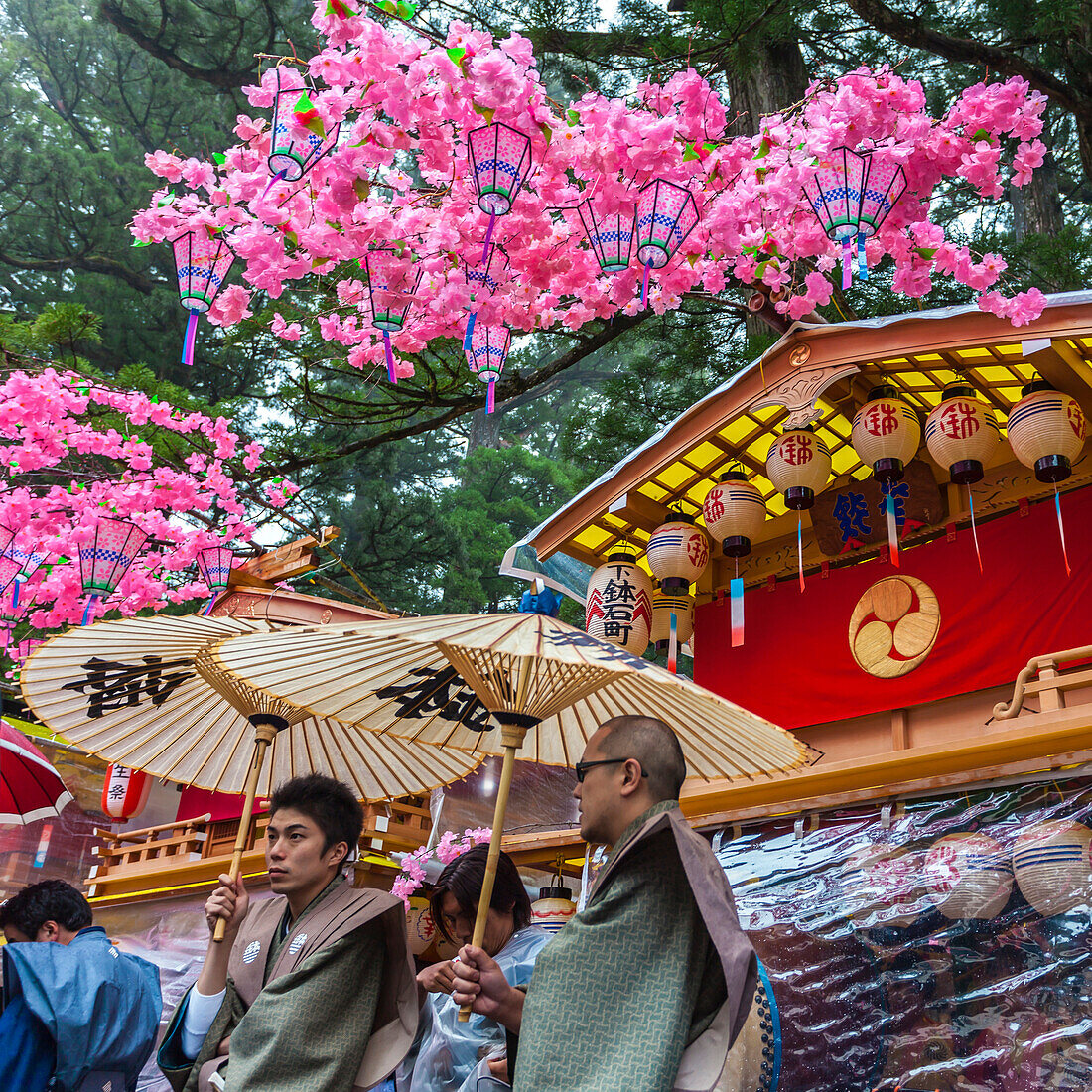Zwei Männer mit Schirmen vor dekorierten Wagen während des Yayoi Matsuri in Nikko, Tochigi Präfektur, Japan