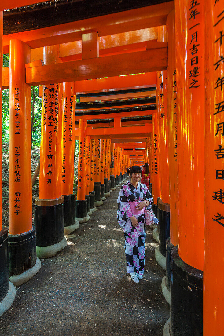 Young woman dressed in kimono at stone path with many red Torii at Fushimi Inari-Taisha in Kyoto, Japan