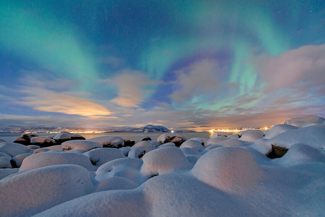 The pink light and the aurora borealis illuminate the snowy landscape on a starry night Strønstad Lofoten Islands Norway Europe.