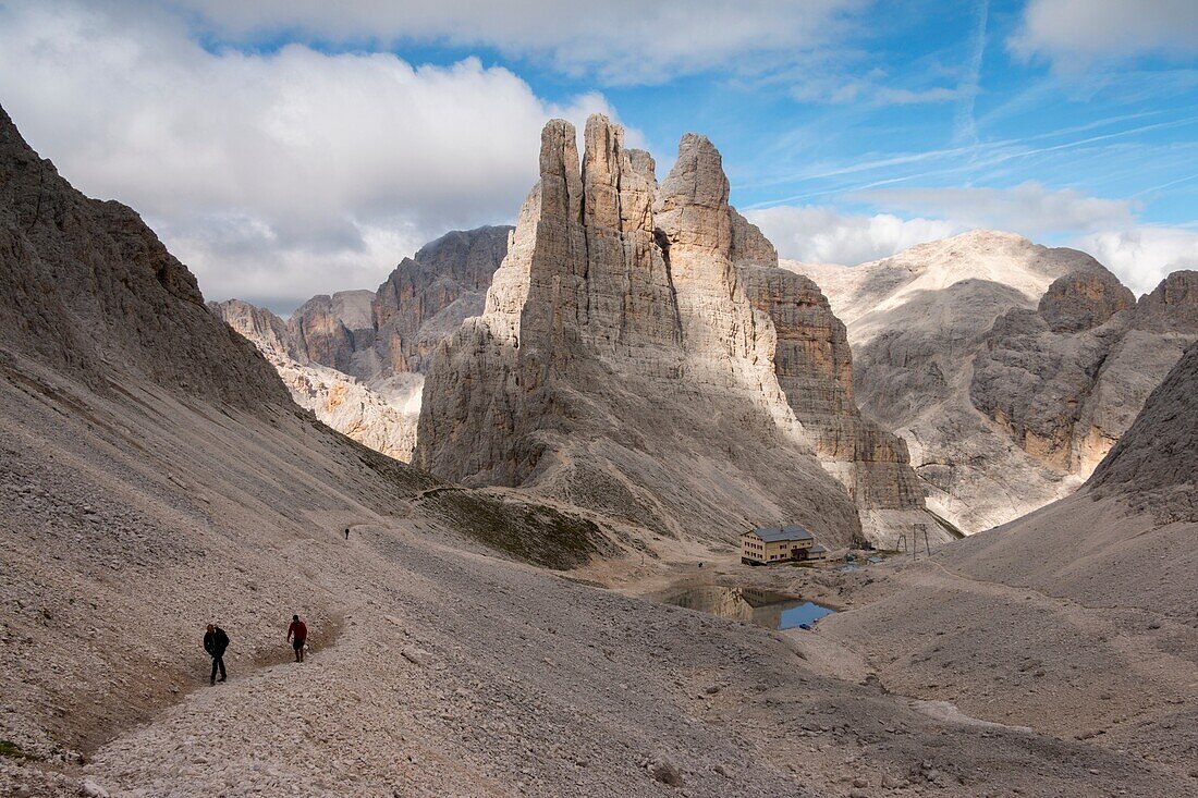 Hikers walking leaving behind Torri del Vajolet and Re Alberto refuge, Dolomites Rosengarten (Catinaccio) group, Trentino Alto Adige, Italy, Europe.