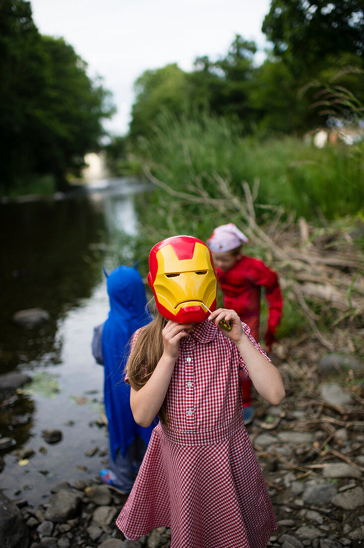 Childhood Games - young girl wearing an IronMan mask : Pre-teen primary school age children playing outdoors on a summer evening, dressed up as comic book superheroes. UK.