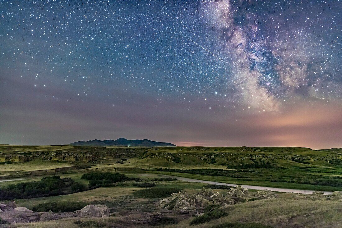 The summer Milky Way with a meteor streaking at centre as a bonus. An aurora to the north off frame is lighting the foreground with a green glow. Haze and forest fire smoke obscure the horizon. I shot this at the Battle Scene viewpoint at Writing-on-Stone