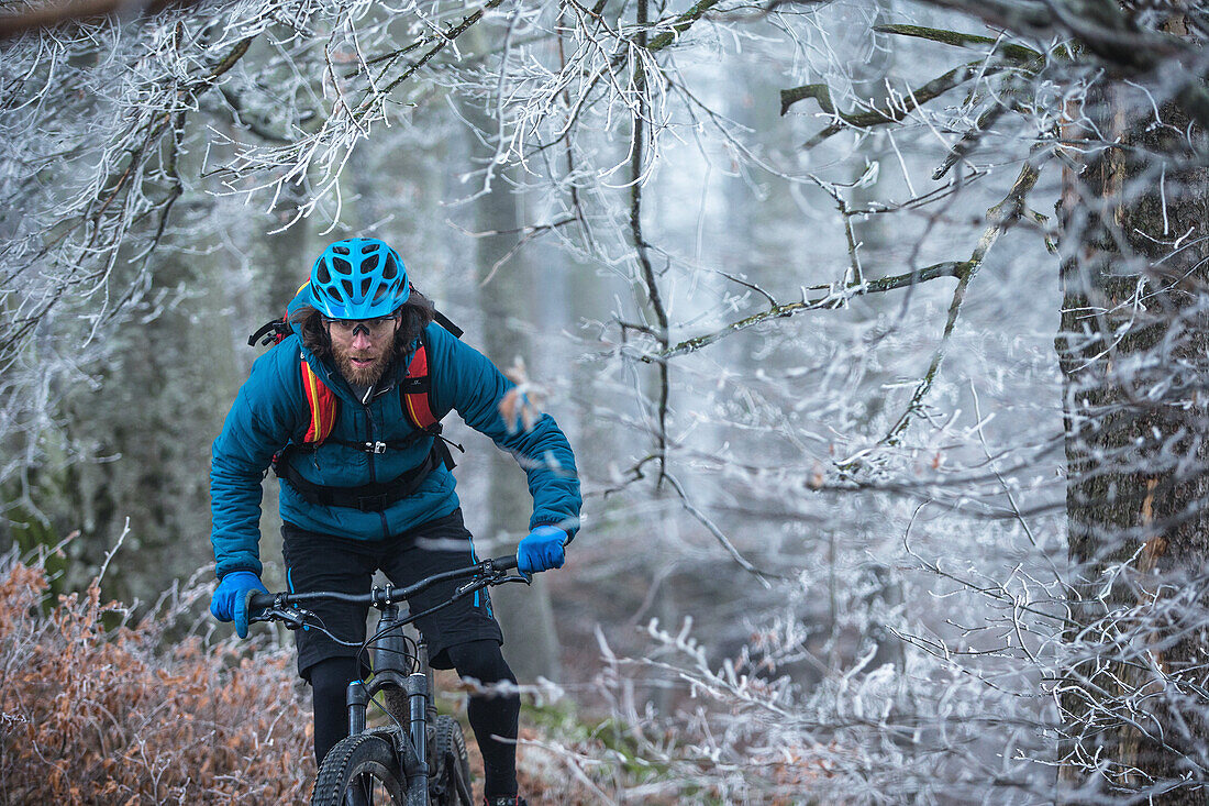 Young man riding with his bike through a with frost covered forest, Allgaeu, Bavaria, Germany