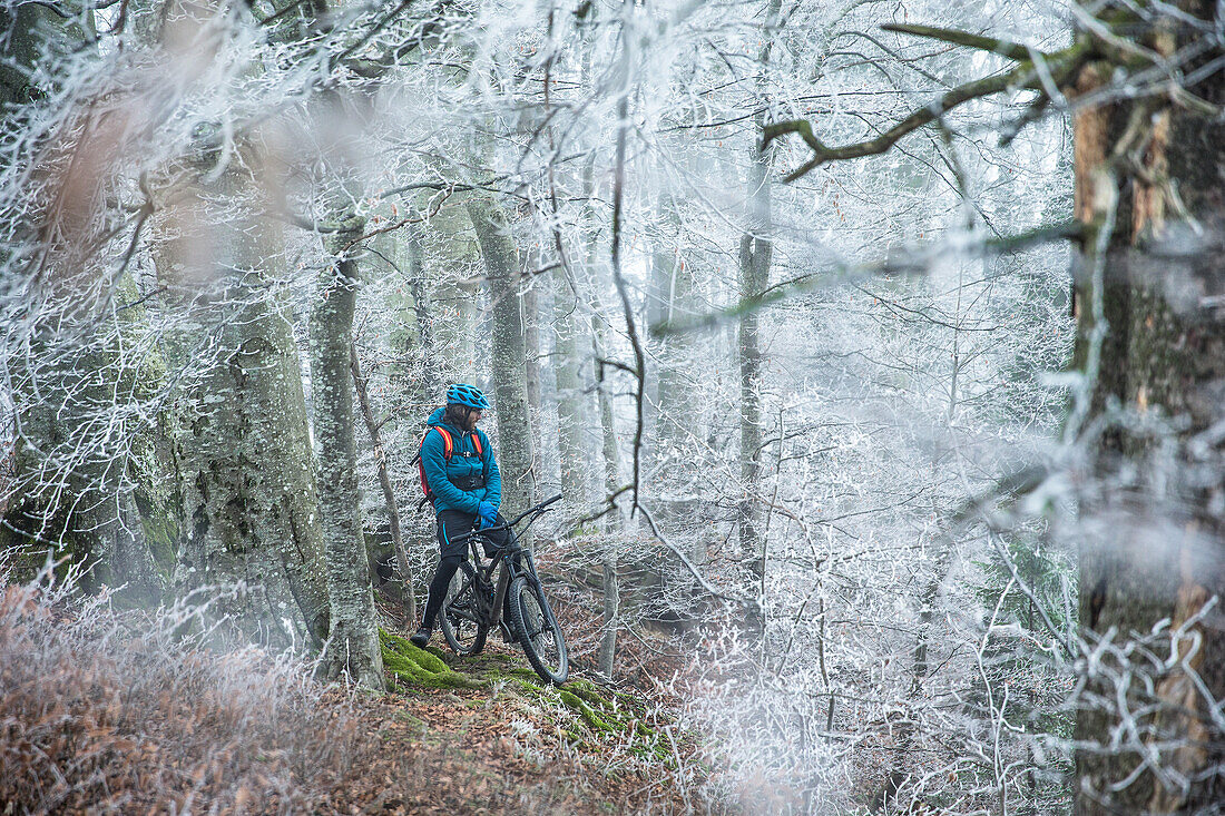 Young man standing with his bike in a with frost covered forest, Allgaeu, Bavaria, Germany