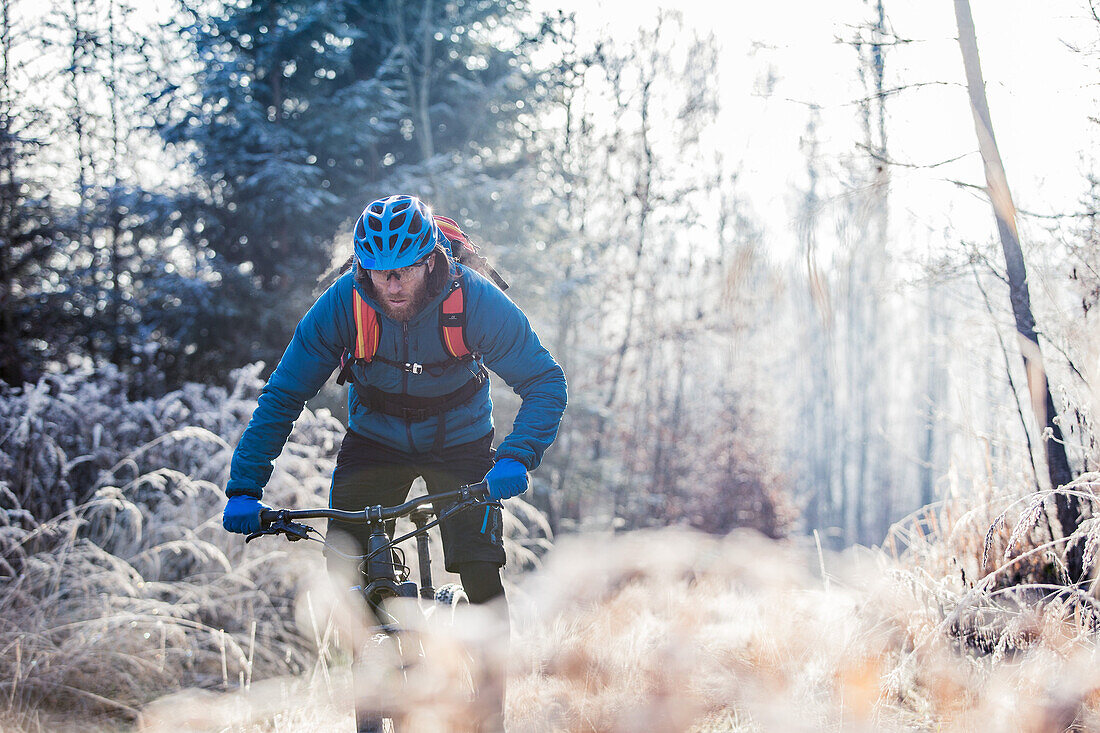 Young man riding with his bike through a with frost covered forest, Allgaeu, Bavaria, Germany