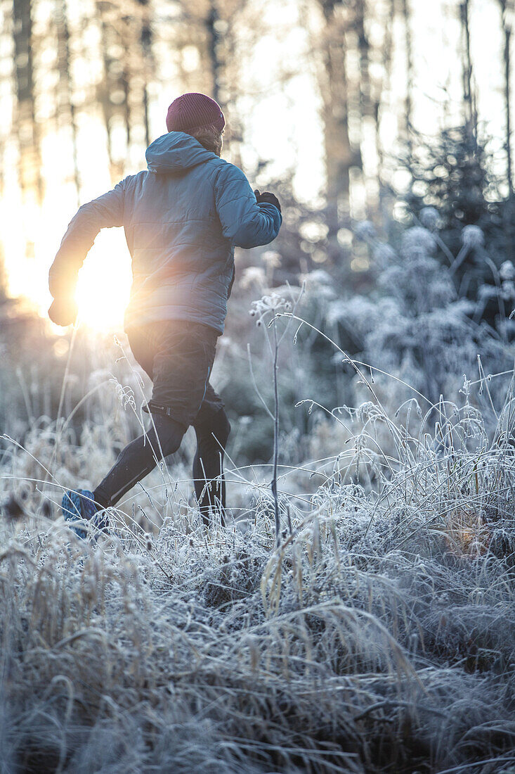 Junger Mann läuft durch einen mit Frost bedeckten Wald, Allgäu, Bayern, Deutschland