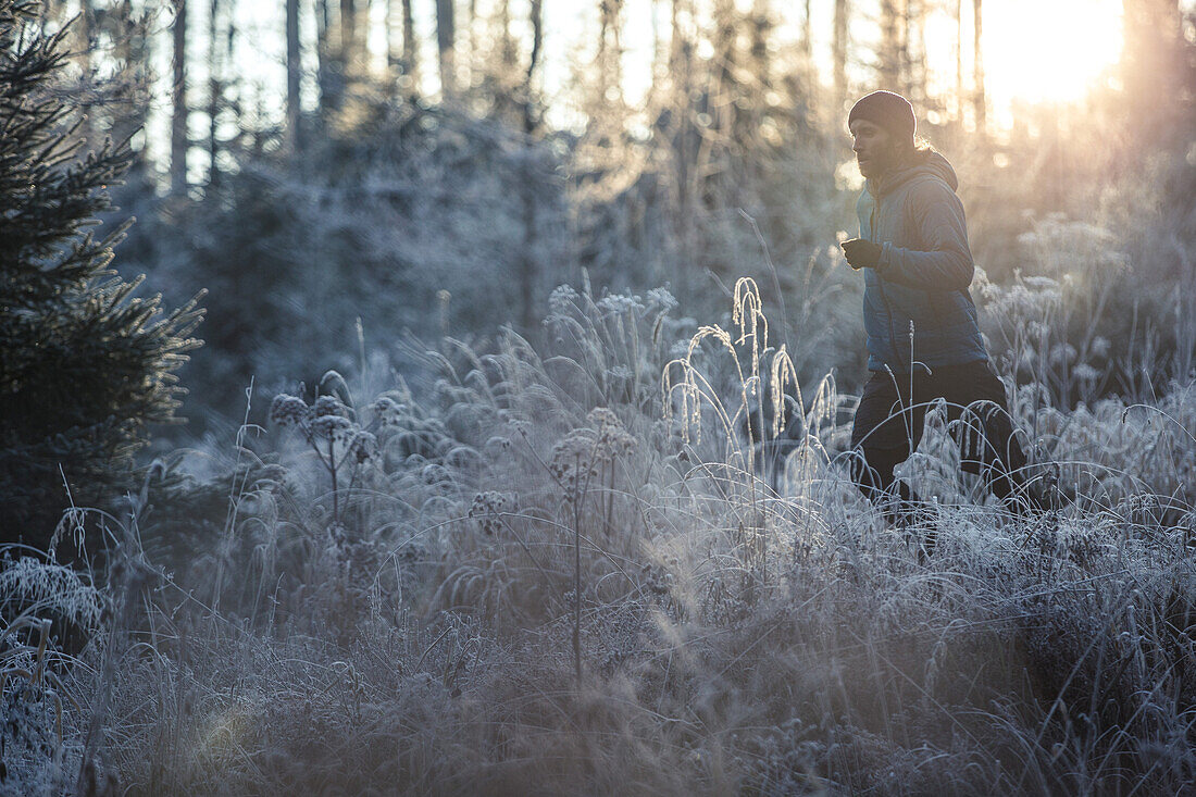 Young man running through a frost covered forest, Allgaeu, Bavaria, Germany