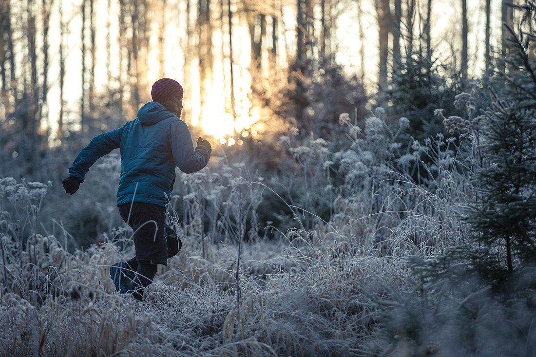 Junger Mann läuft durch einen mit Frost bedeckten Wald, Allgäu, Bayern, Deutschland