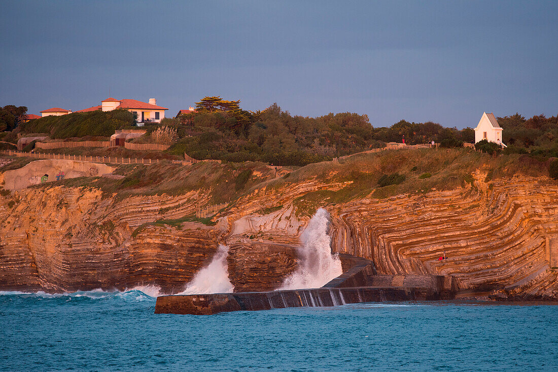 Waves crash against rocky coastline at sunset