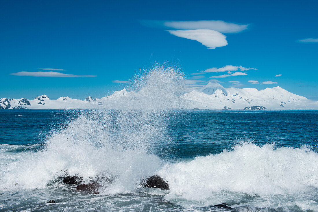 Waves crash ashore with snow-covered mountains behind