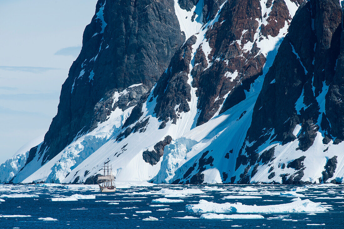 Segelschiff Europa (eine Bark) navigiert durch Eisschollen mit schneebedeckte Berge im Hintergrund, Lemaire-Kanal, nahe Grahamland, Antarktische Halbinsel, Antarktis