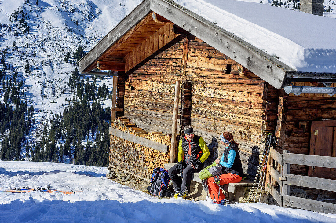 Frau und Mann auf Skitour sitzen an Almhütte und machen Pause, Tuxer Alpen, Tirol, Österreich