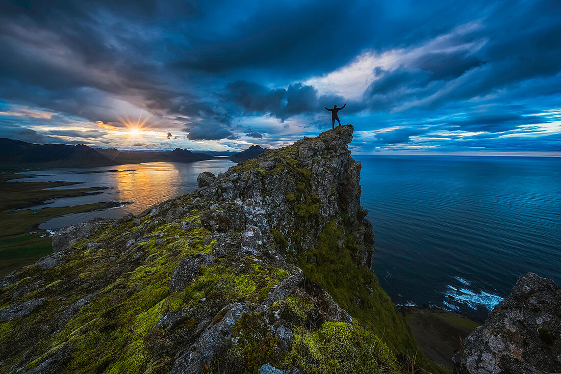 'Man standing on top of a sea cliff at sunset along Iceland's Strandir Coast in the West Fjord region; Iceland'