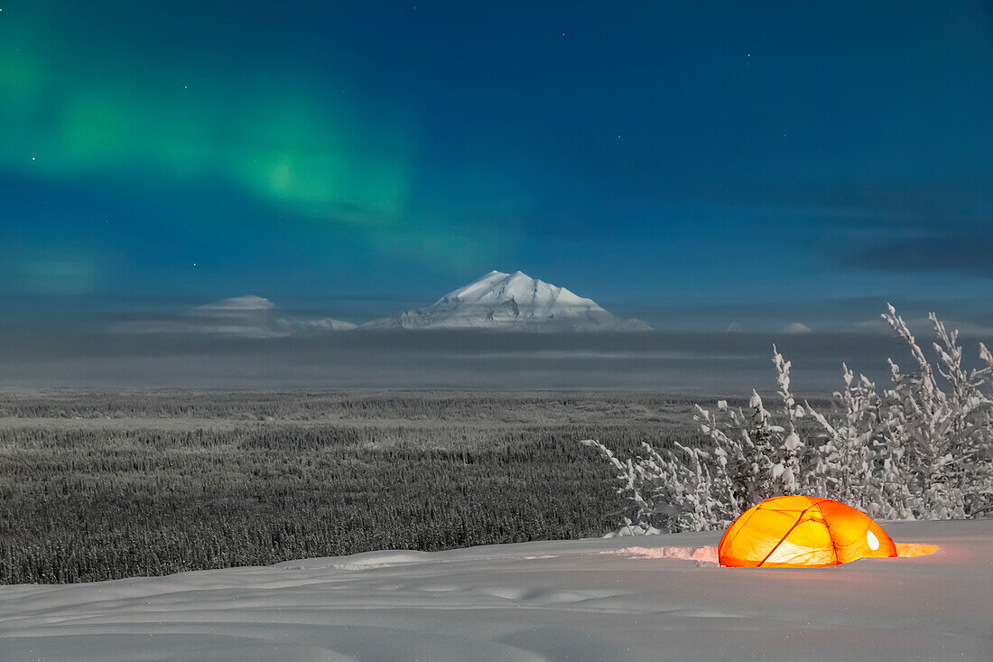 'Green Aurora Borealis shines above moonlight casting light on Mount Drum and the Copper River Valley, a glowing tent on a foggy winter night, Copper River Valley, South-central Alaska; Alaska, United States of America'