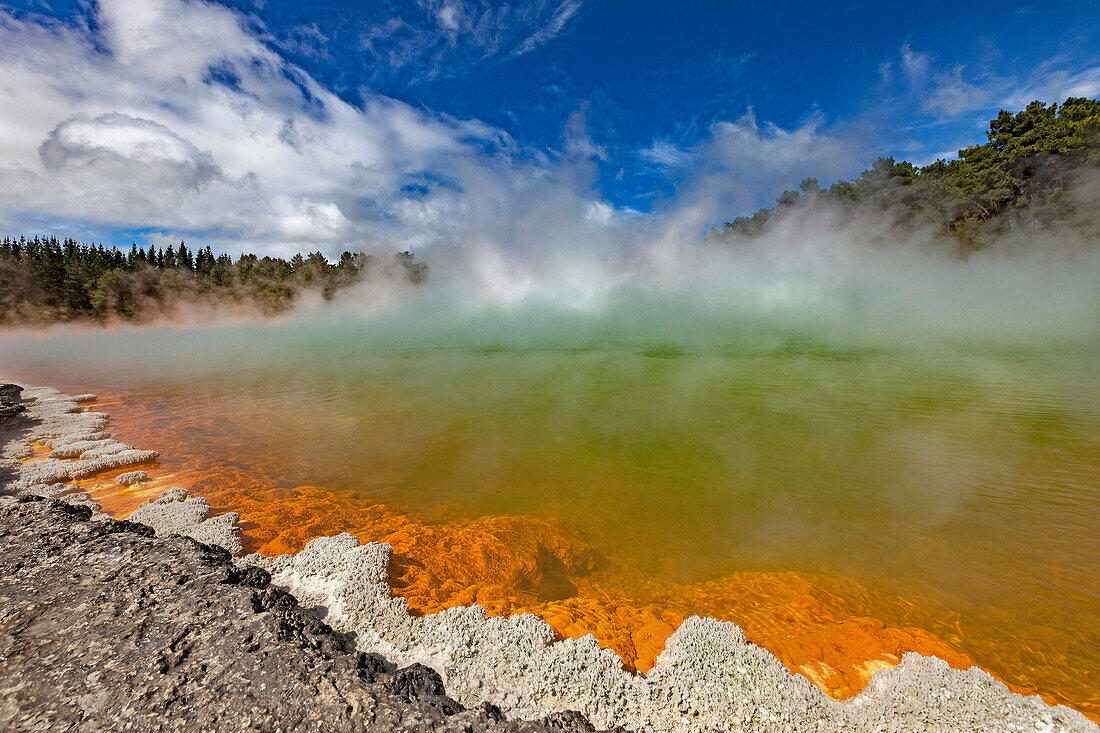 Champagne pool, burst of sunshine lights up foreshore during day of blowing mist and heavy rain, Wai-o-Tapu thermal region, Rotorua.