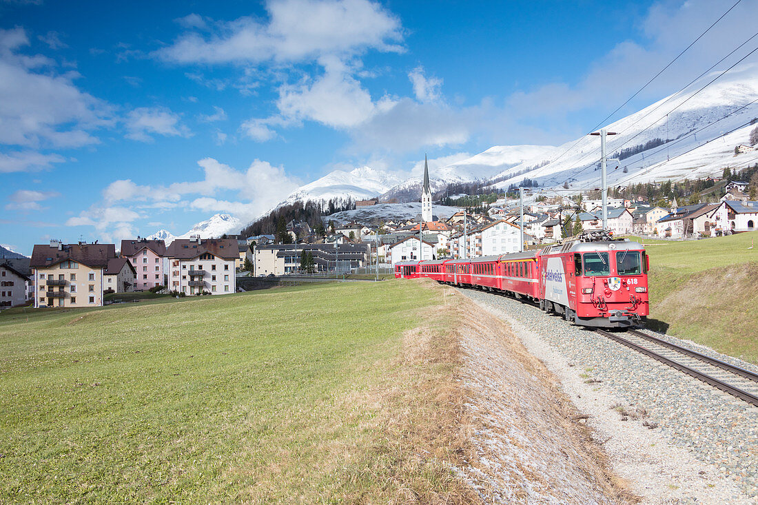 The red train runs across the alpine village of Zuoz in spring, Maloja, Canton of Graubunden, Engadine, Switzerland, Europe