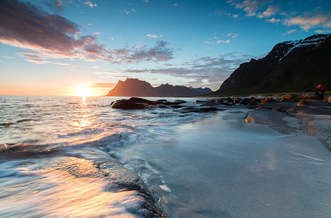 Pink clouds and midnight sun reflected on the waves of blue sea framed by rocky peaks, Uttakleiv, Lofoten Islands, Norway, Scandinavia, Europe