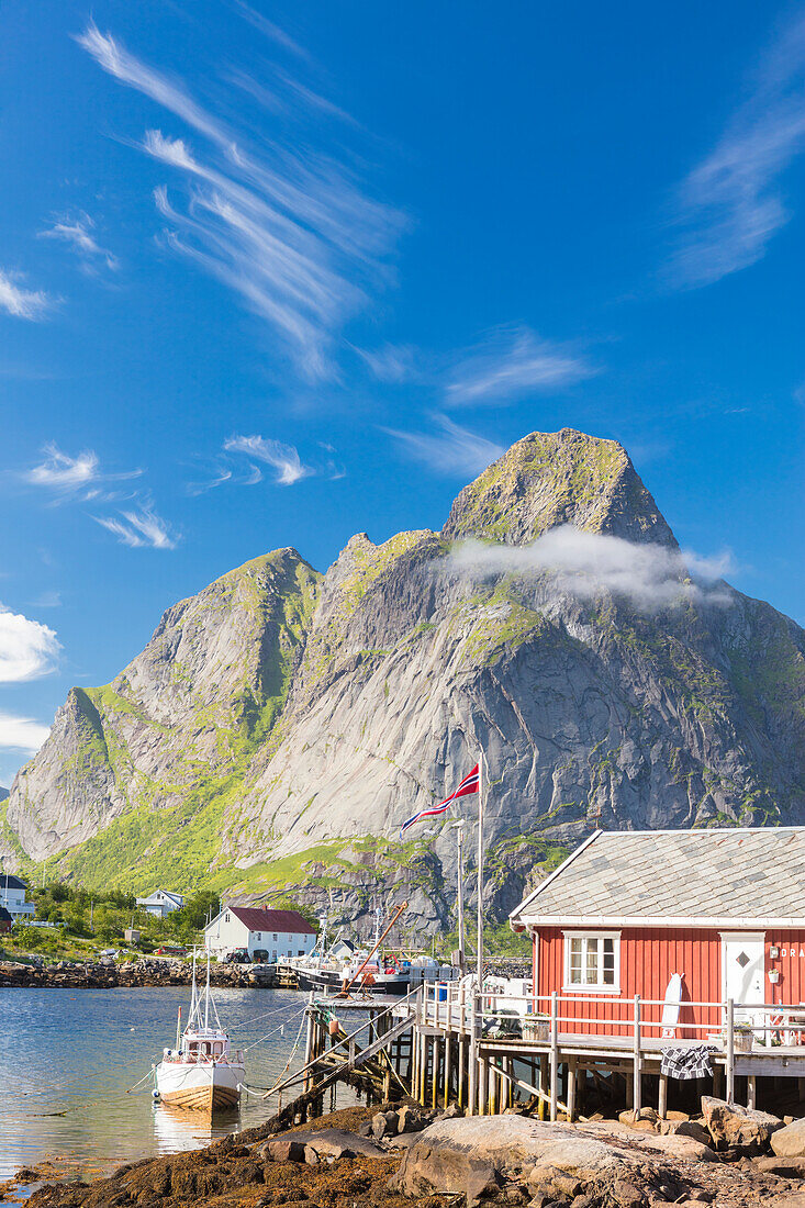Typical house of fishermen called Rorbu framed by rocky peaks and blue sea, Reine, Moskenesoya, Lofoten Islands, Norway, Scandinavia, Europe