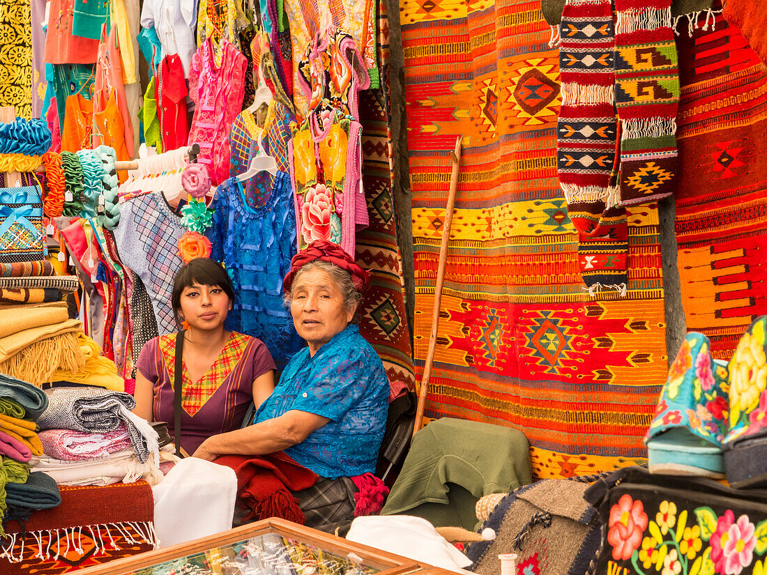Women talking in market with background of handmade rugs and clothing, Oaxaca, Mexico, North America