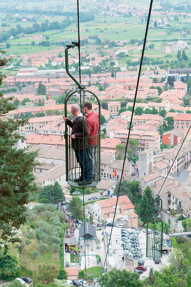 Europe, Italy, Umbria, Gubbio, two people in a cable car with Gubbio town in the background