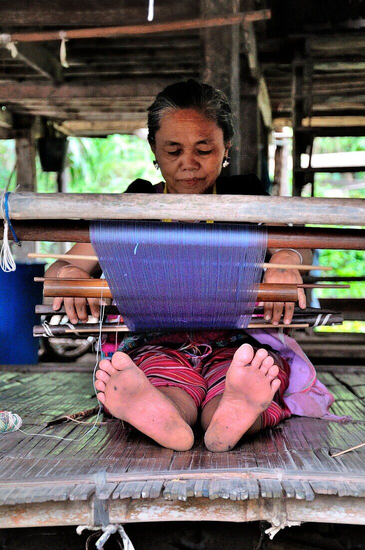 woman weaves in his hut in the Thai jungle