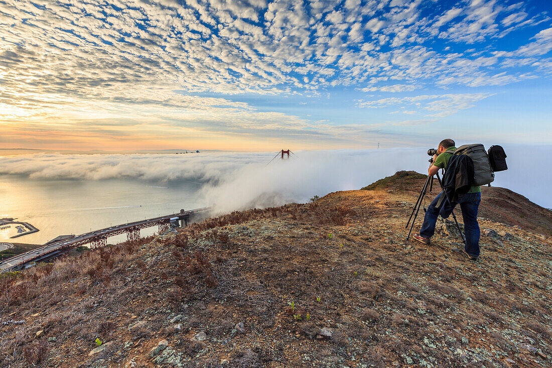 A photographer takes pictures of Golden Gate Bridge at sunrise from Slackers Hill, San Francisco, Marin County, California, USA