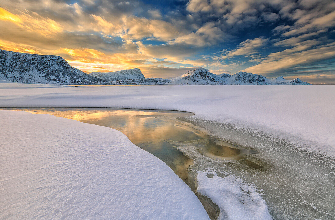 The golden sunrise reflected in a pool of the clear sea where the snow is almost melted, Haukland Lofoten Islands Norway Europe