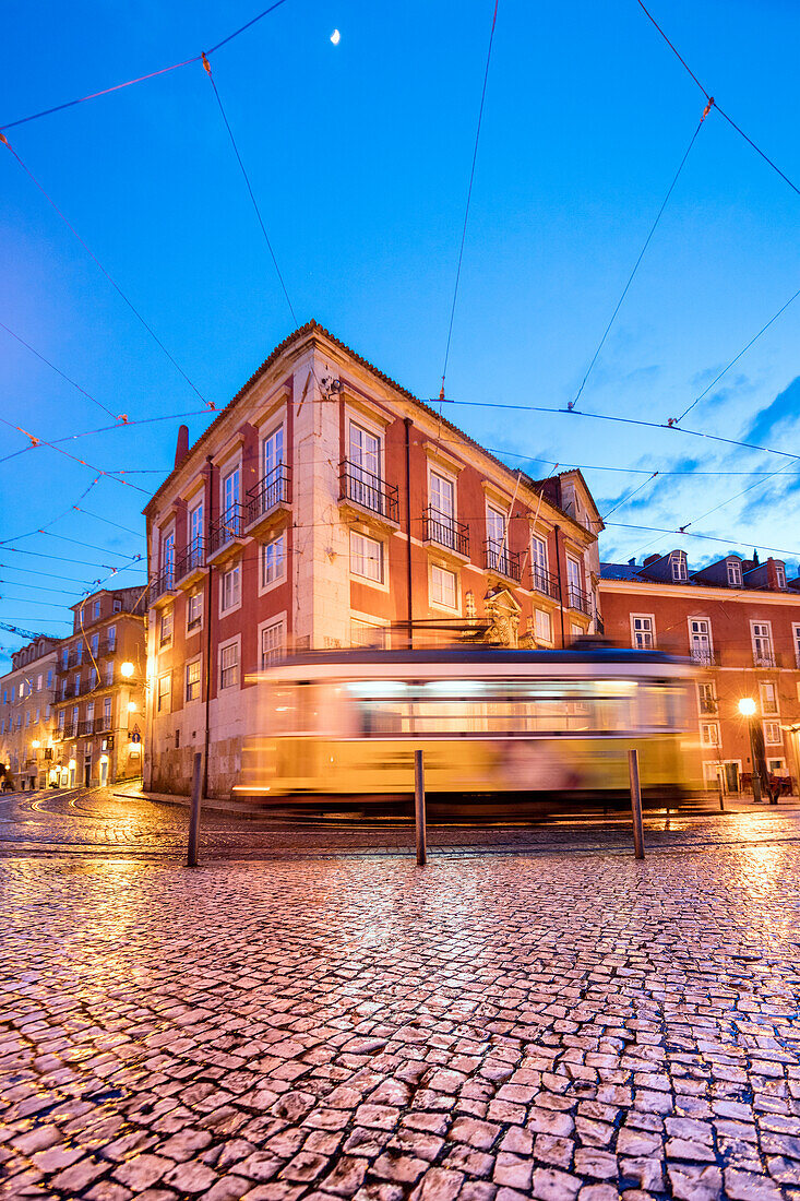 City lights on the typical architecture and old streets at dusk while the tram 28 proceeds Alfama Lisbon Portugal Europe