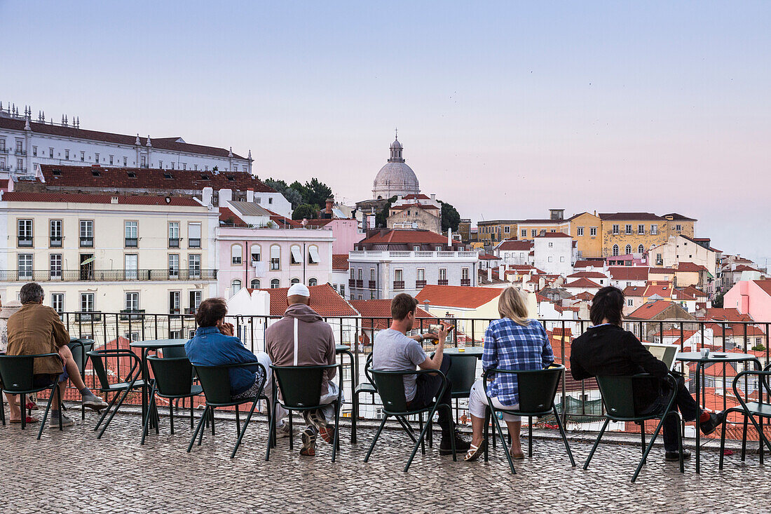 Tourists admire terracotta roofs and ancient dome from a terrace at Miradouro Alfama viewpoint of Lisbon Portugal Europe