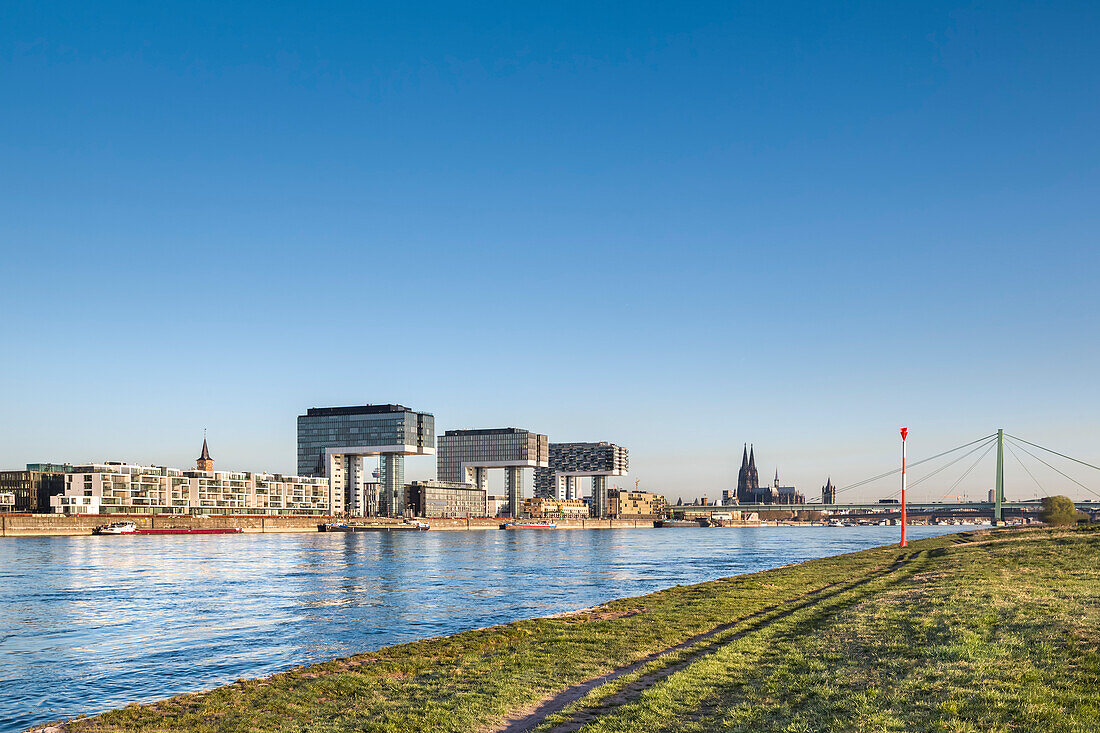 View over river Rhein towards Rheinau harbour with crane houses, Cologne Cathedral, Cologne, North Rhine-Westphalia, Germany