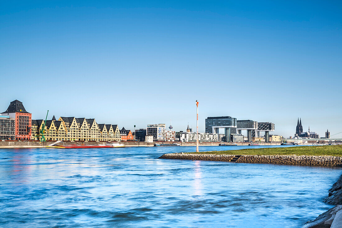 View over river Rhein towards Rheinau harbour with crane houses, Cologne Cathedral, Cologne, North Rhine-Westphalia, Germany