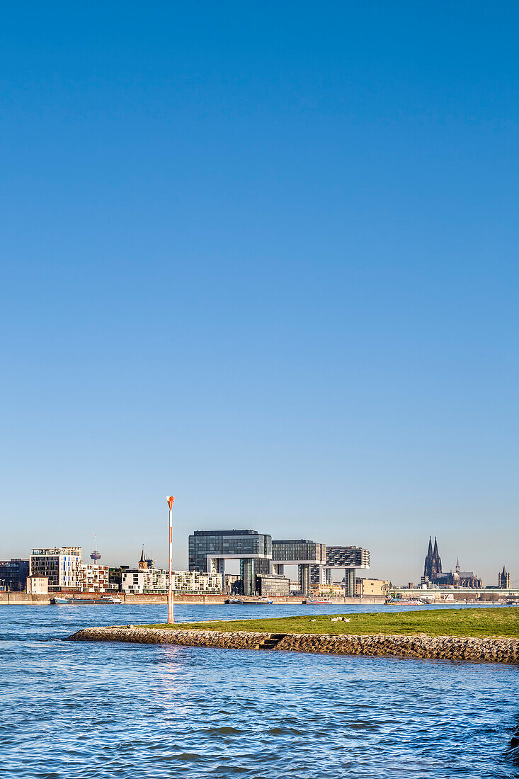 View over river Rhein towards Rheinau harbour with crane houses, Cologne Cathedral, Cologne, North Rhine-Westphalia, Germany