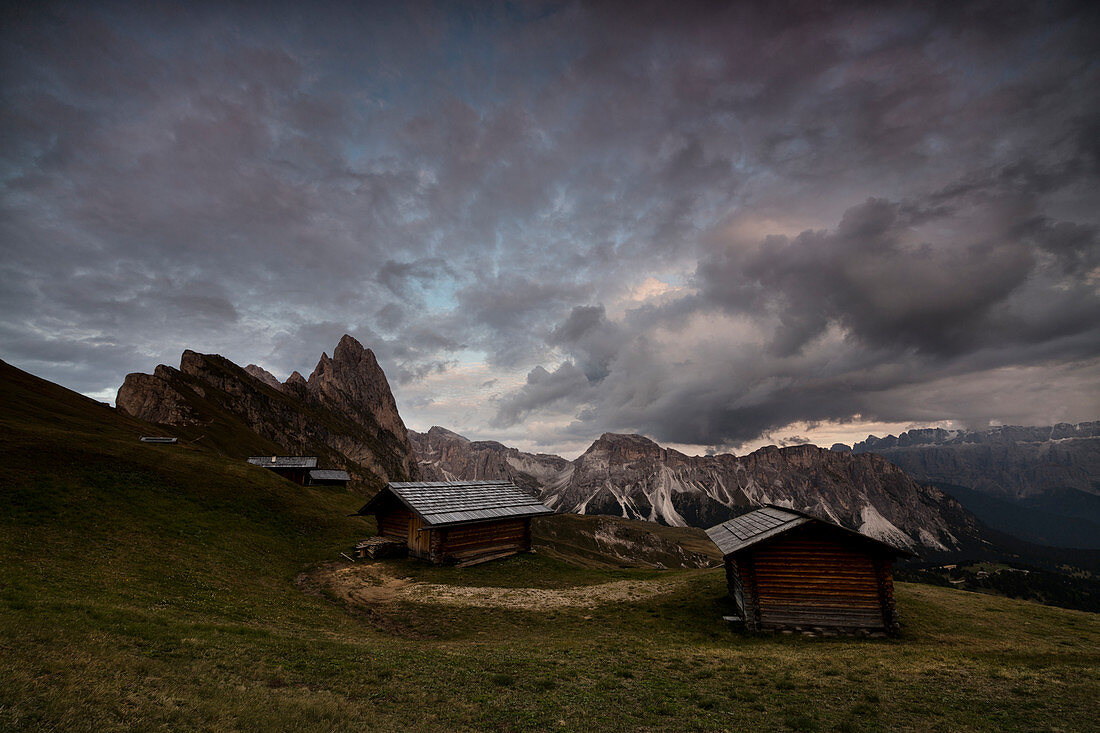 Dark clouds on green meadows and huts of the Odle mountain range seen from Seceda, Val Gardena, Trentino-Alto Adige, Italy, Europe