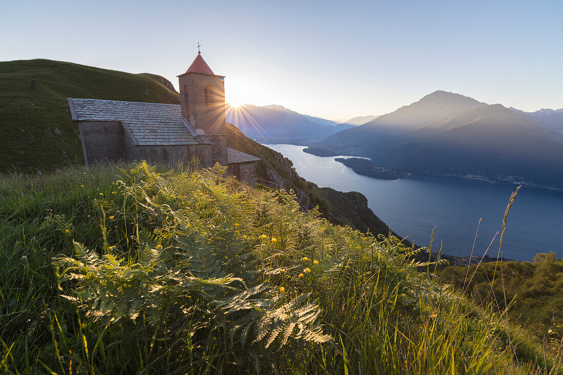 Sunbeam on Church of San Bernardo lights up the landscape around the blue water of Lake Como at dawn, Musso, Lombardy, Italy, Europe