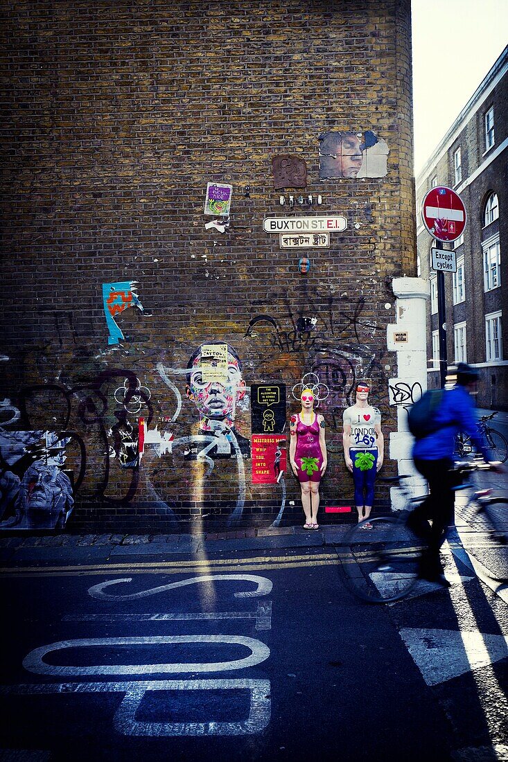 Un ciclista irreconocible circulando por una calle y en la pared de fondo pintada con graffitis. Buxton St. East End, London, UK, Europa.