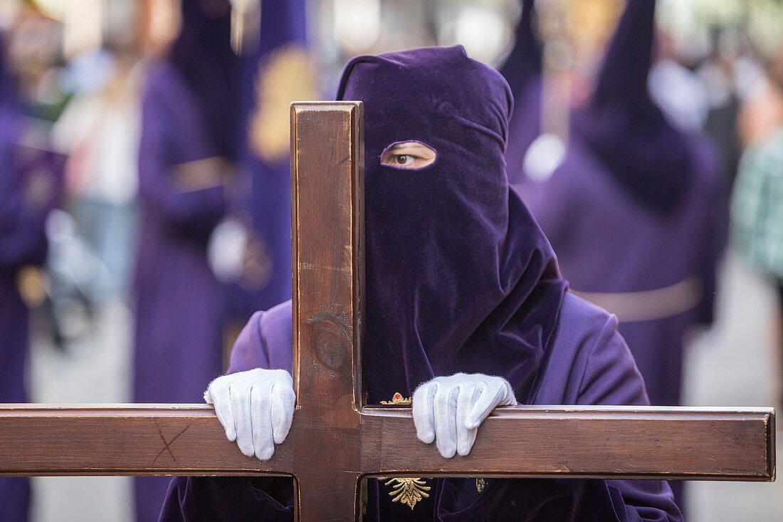 Penitent dressed in purple tunic of velvet resting on wooden cross during atonement station on Holy Week, Andalusia, Spain.