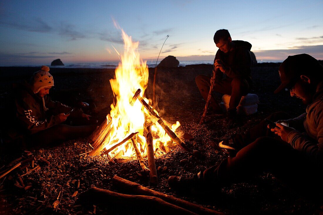 Trevor Avery of the Yurok Indian Tribe, Anthony Henry, and Lonnie Risen Jr. , of the Hoopa Valley Tribe (from left) sit by a driftwood campfire while fishing for lamprey at the mouth of the Klamath River on the Pacific Ocean on February 24, 2015. Yurok In