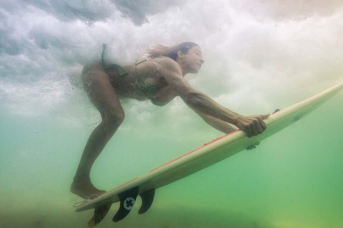 Woman with surf board under a wave.