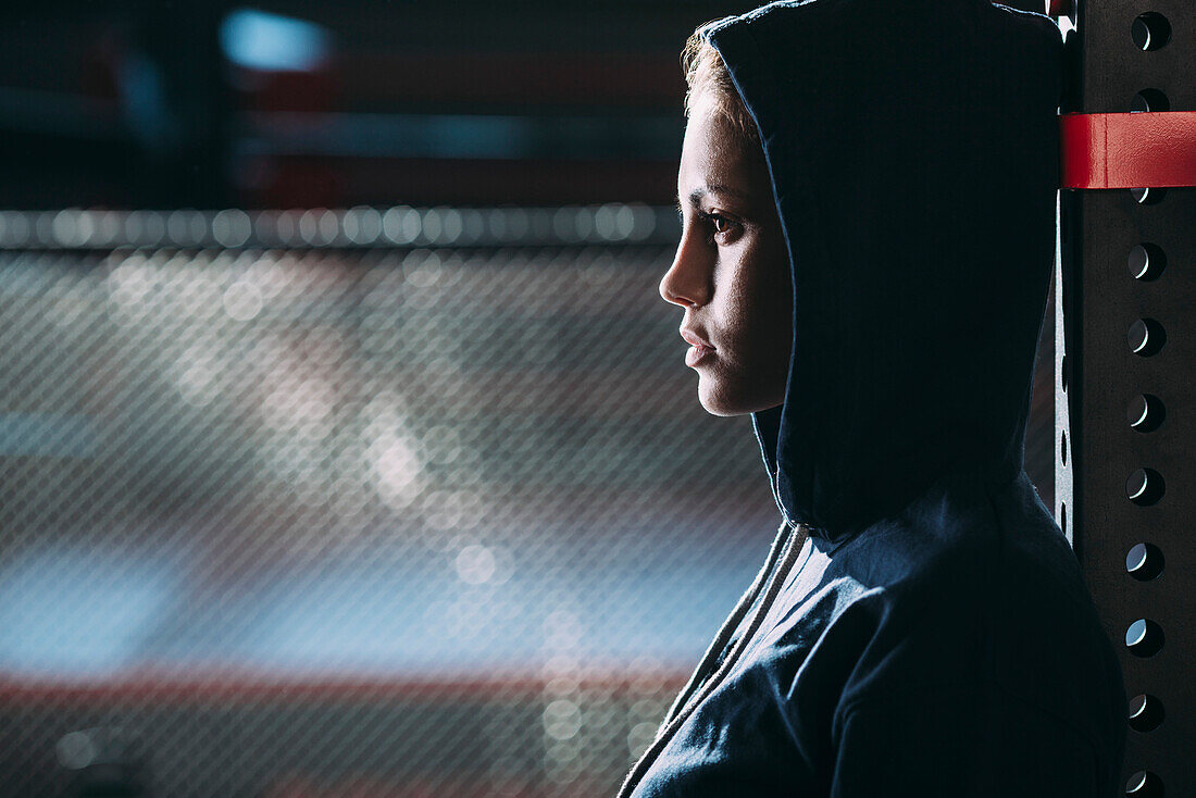 Close-up side view of woman wearing hooded shirt standing at gym