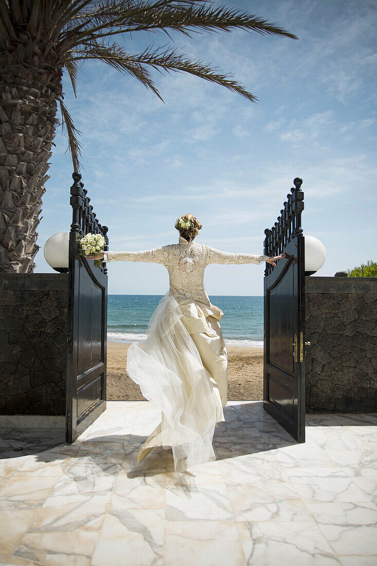 Rear view of bride opening gate while walking towards beach